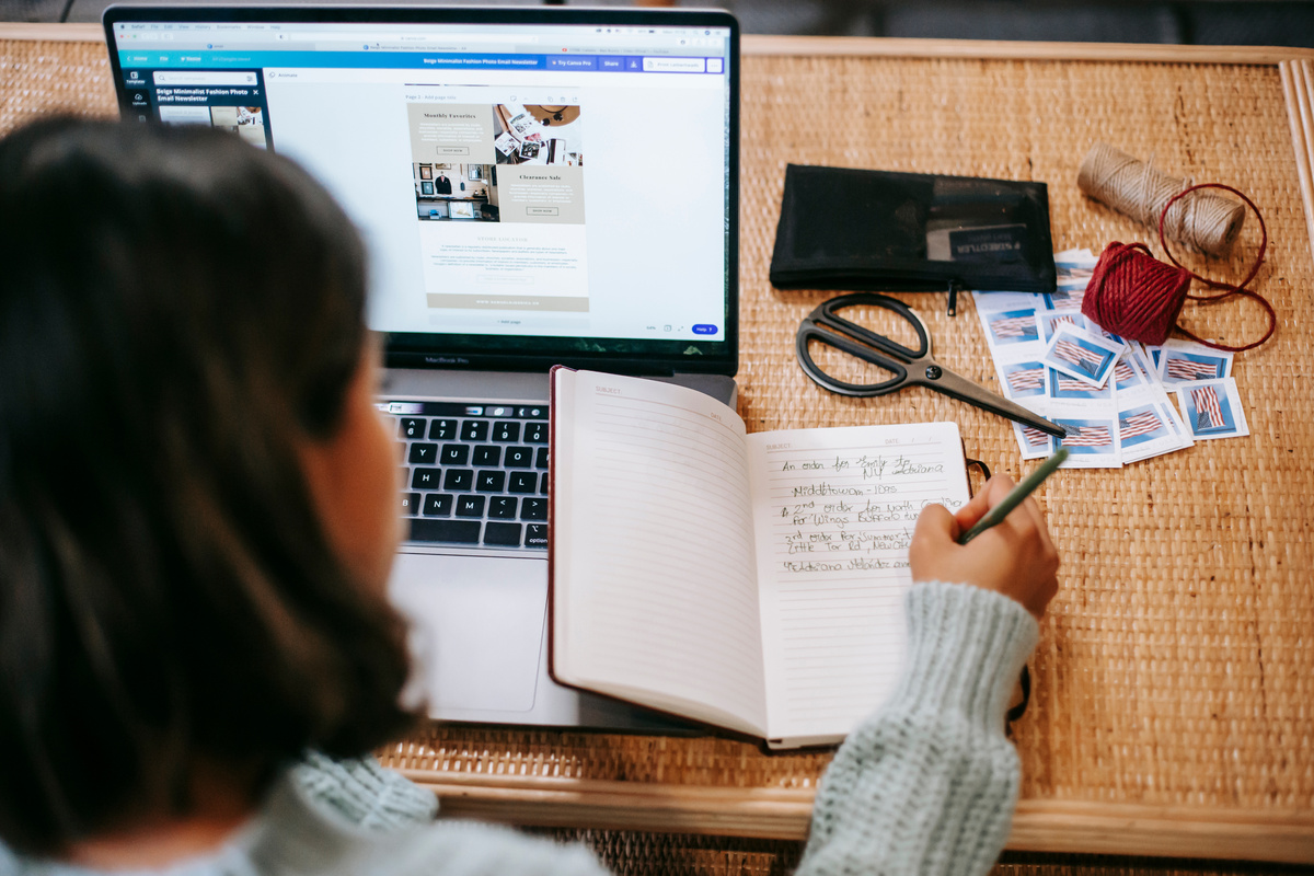 Unrecognizable ethnic female student taking notes in notebook near laptop